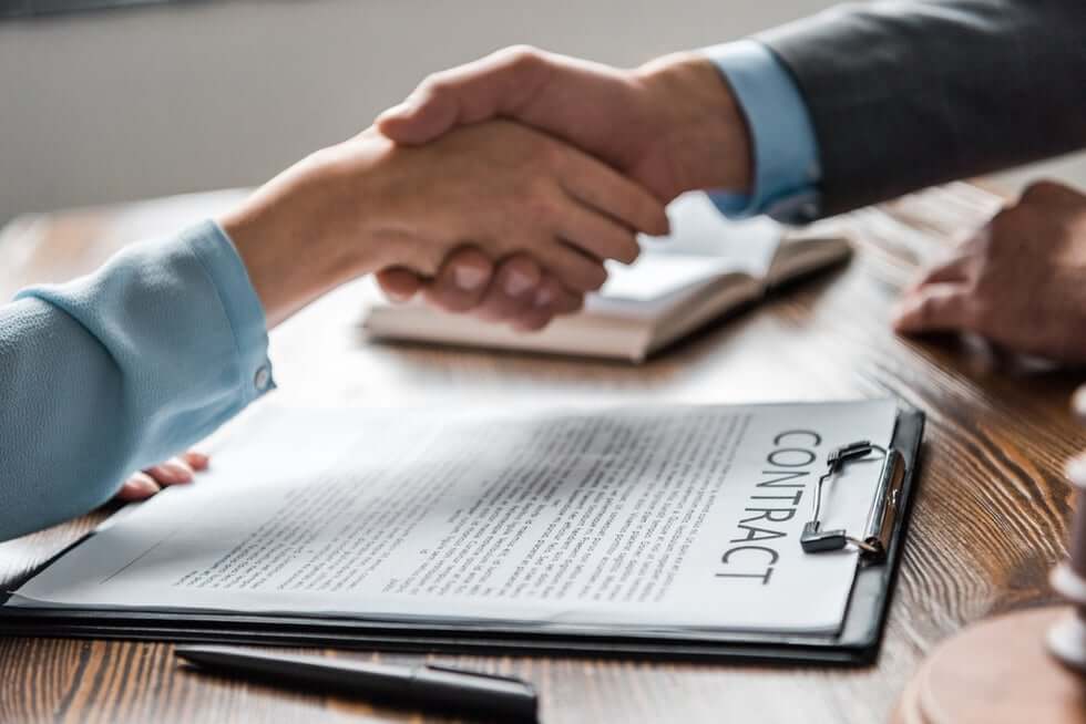 Business partners shaking hands over clipboard with signed partnership contract