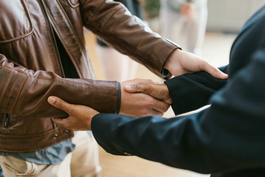 Person in black suit shaking hands with a person in brown leather jacket