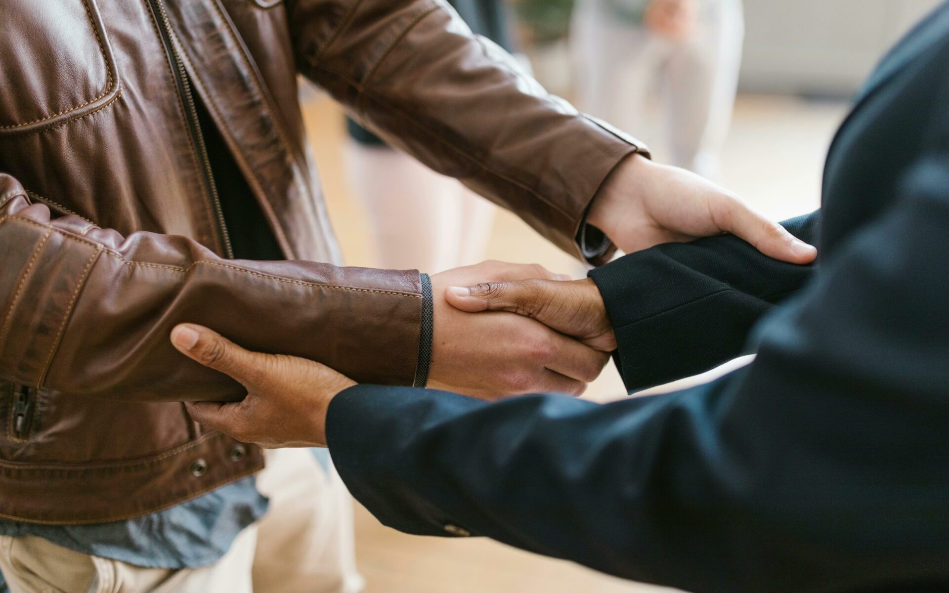 Person in black suit shaking hands with a person in brown leather jacket