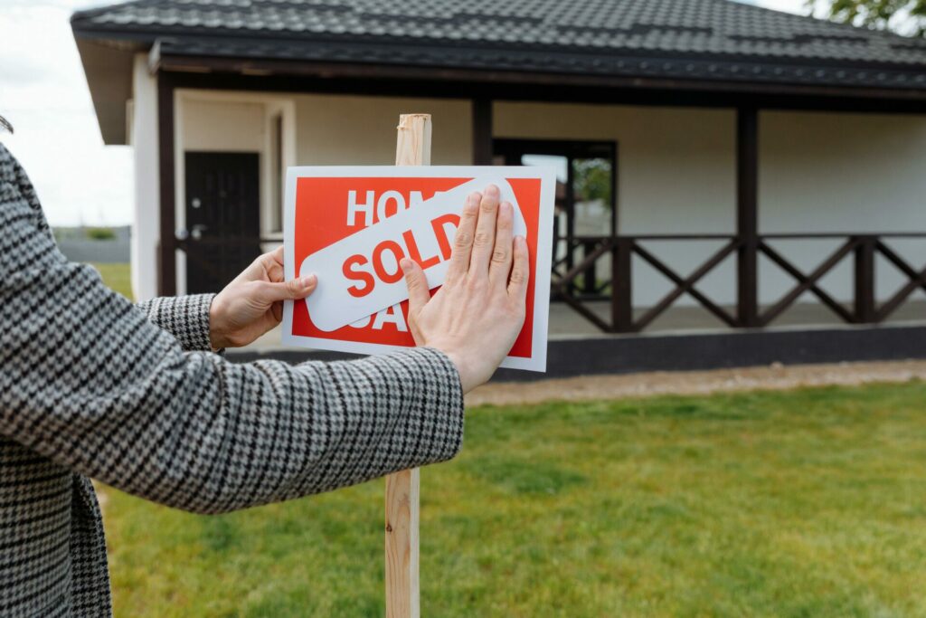 a person putting a SOLD sticker above the House for Sale signage