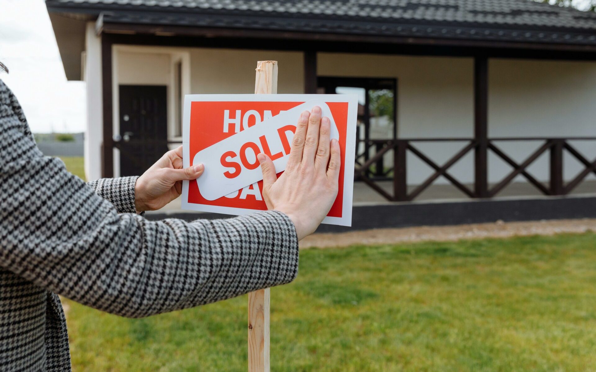 a person putting a SOLD sticker above the House for Sale signage