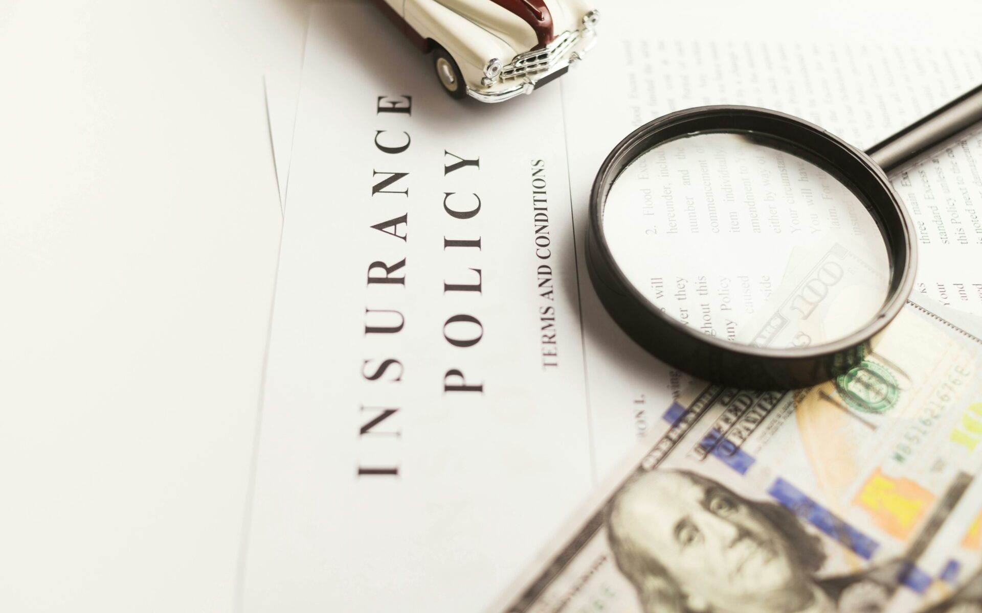 A toy car, magnifying glass and us dollar bills on top of an insurance policy document